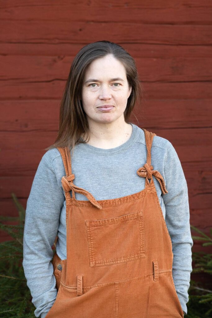 Porträttbild av Martha Kristensen ståendes framför faluröd vägg, tittar i kameran