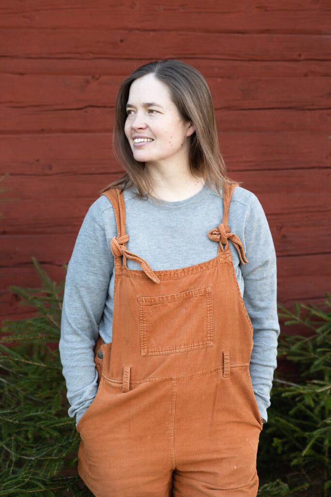 Porträttbild av Martha Kristensen ståendes framför faluröd vägg, tittar åt sidan