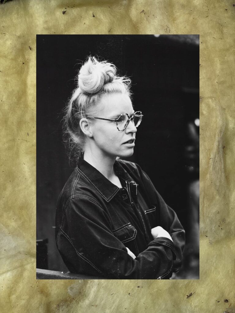 Svartvitt porträttfoto av Rebecka Bebben Andersson med ram av gul glasfiberisolering, stående format