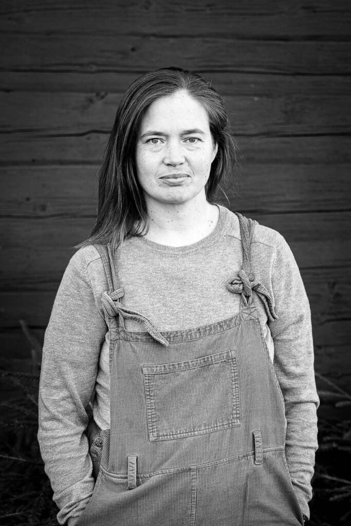 Svartvit porträttbild av Martha Kristensen ståendes framför mörk vägg, tittar i kameran